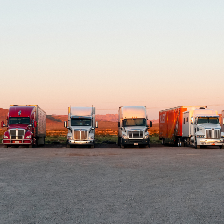 En la imagen se muestra cuatro camiones estacionados con el atardercer detrás