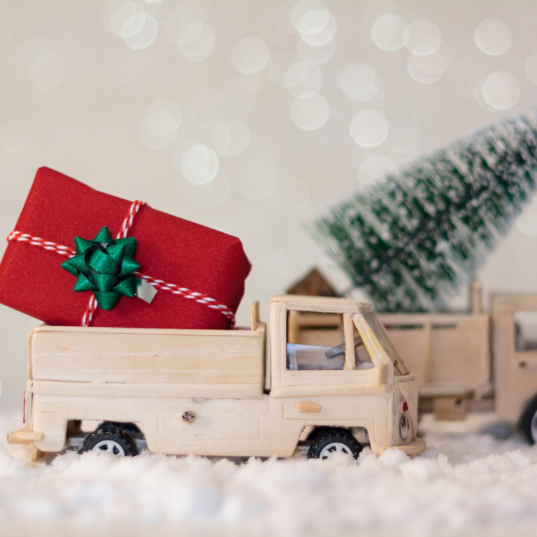 En la imagen se observan dos camiones de madera cargando un regalo y un pino de Navidad
