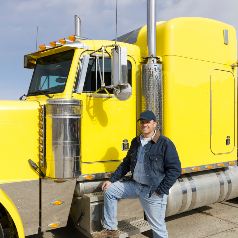 En la imagen se observa un camionero feliz apoyando su pie en el escalón de un camión amarillo