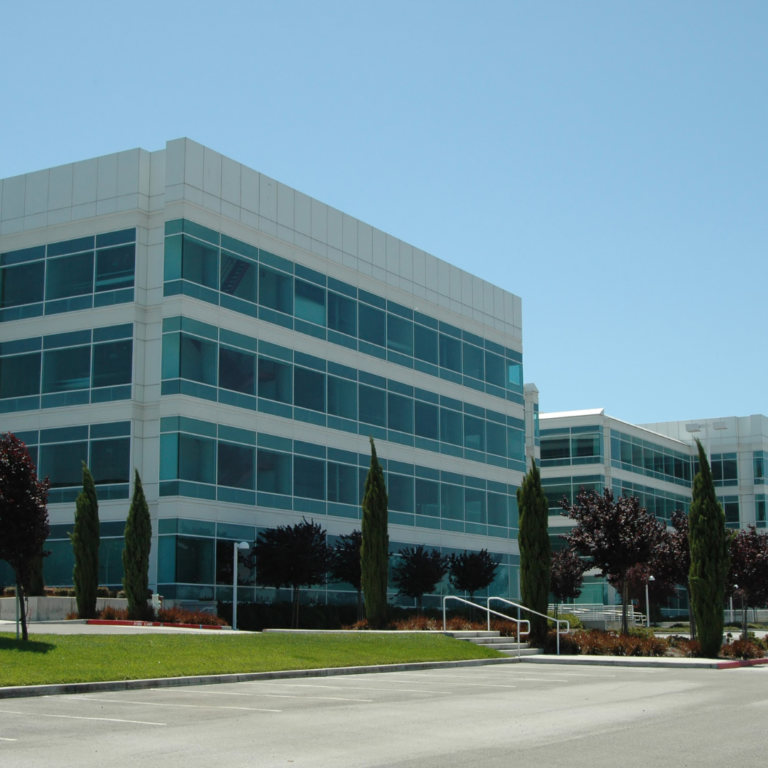 En la imagen se observa la sede de Silicon Valley, un edificio blanco con ventanas, rodeado de árboles