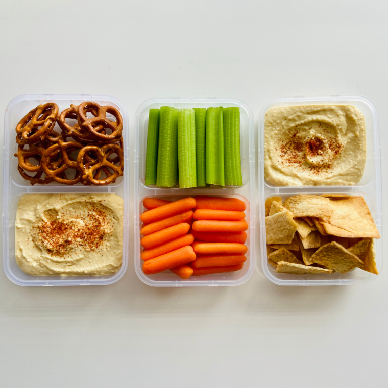 En la imagen se muestran contenedores con zanahoria, apio, pretzels, tostadas y hummus