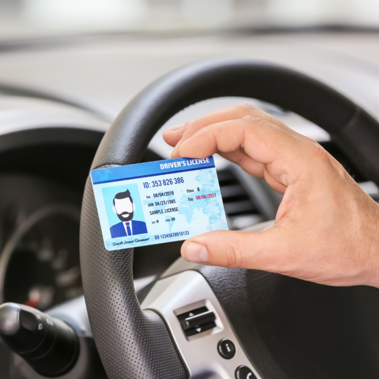 En la imagen se muestra una mano sosteniendo una licencia de conducir, frente a un volante de auto
