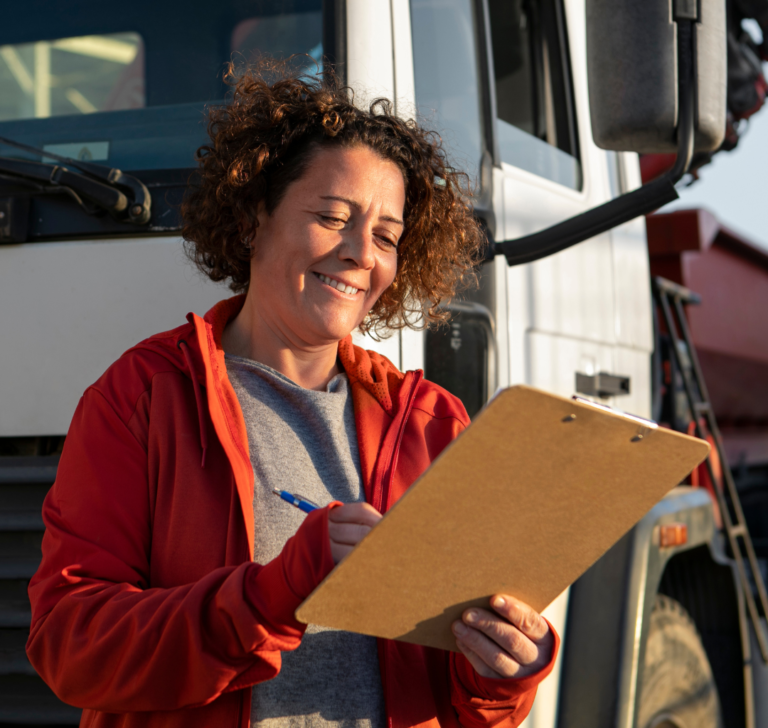 En la imagen se muestra una mujer sonriendo llenando papeles frente a un camión