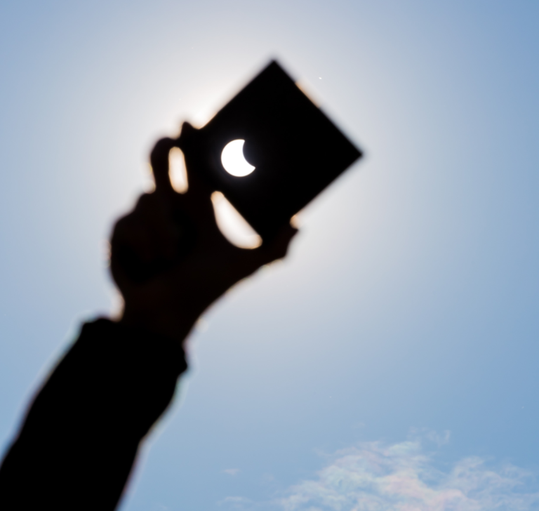 En la imagen se muestra una mano sosteniendo un cartón para ver un eclipse solar