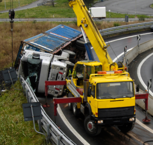 En la imagen se muestra un camión volteado tras un accidente y una grúa remolcándole